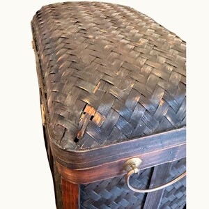 May include: A dark brown woven trunk with a curved top. The trunk has a rectangular shape with a dark brown wooden frame and a metal handle. The woven material has a textured appearance with visible wear and tear.