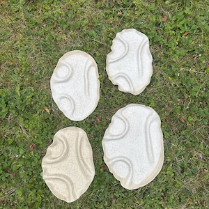 May include: Four irregular, oval-shaped ceramic trays with a speckled, off-white finish. Each tray features a unique, undulating surface with raised, curved ridges that create organic, wave-like patterns across the textured, matte surface.