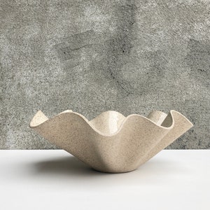 May include: A large, white ceramic bowl with a wavy, ruffled edge. The bowl has a speckled, textured surface.