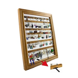 May include: A wooden framed earring display with a light brown finish. The display is filled with various earrings of different colors and styles. The display has multiple rows of small holes to hang earrings. A small stand is attached to the back.