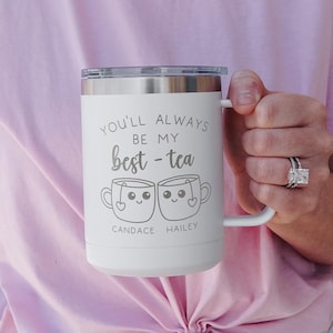 May include: White stainless steel travel mug with a black handle. The mug has the text "You'll always be my best-tea" with two cartoon teacups with faces and the names "Candace" and "Hailey" underneath.