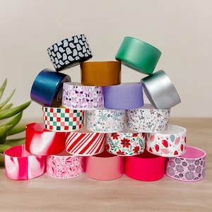 Puede incluir: Una pila de tapas de tarro de velas coloridas y estampadas. Las tapas son de metal y plástico y presentan varios diseños, incluyendo fantasmas, flores y rayas.