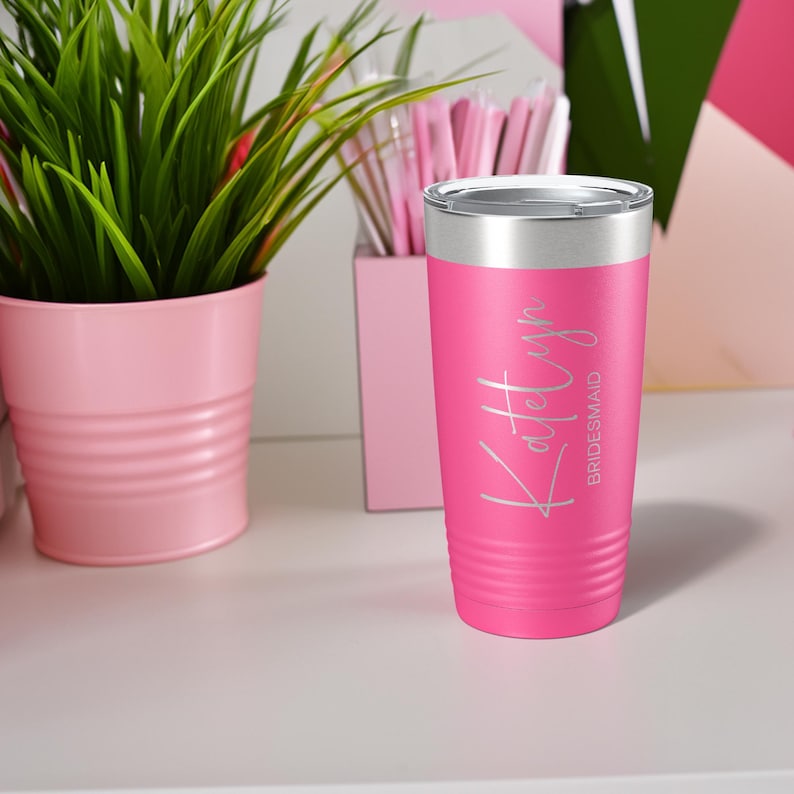 May include: Pink stainless steel tumbler with a silver lid. The tumbler has the name "Katelyn" and the word "bridesmaid" engraved on it.