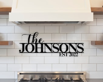 May include: Black metal sign with the text "The Johnsons Est 2022" mounted on a white tiled kitchen backsplash.