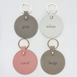 Pu&ograve; includere: Quattro portachiavi rotondi in grigio, bianco, corallo e beige. Ogni portachiavi ha un anello color oro e un cinturino abbinato con un bottone a pressione dorato. I colori sono etichettati su ogni portachiavi.
