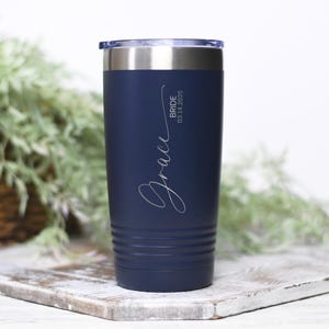 May include: A navy blue stainless steel tumbler with a white inscription that reads "Grace Bride 03.14.2025".