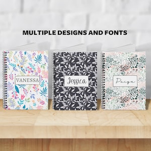 May include: Three personalized spiral notebooks with different floral designs. The notebooks are white with colorful floral patterns, black with gray floral patterns, and pink with green floral patterns. The names "Vanessa", "Jessica", and "Paige" are printed on the front of each notebook.