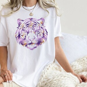 May include: A white t-shirt featuring a purple and gold tiger head graphic print.