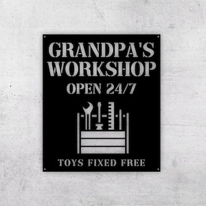 May include: Black metal sign with white text that reads "Grandpa's Workshop Open 24/7" and "Toys Fixed Free". A toolbox with tools is pictured in the center.