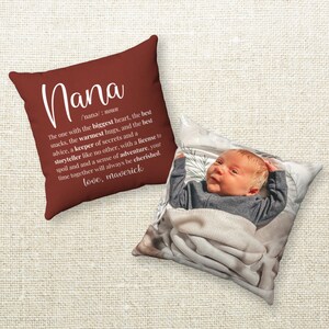 May include: A red throw pillow with white text that reads "Nana /nana/: noun The one with the biggest heart, the best snacks, the warmest hugs, and the best advice, a keeper of secrets and a storyteller like no other, with a license to spoil and a sense of adventure, your time together will always be cherished. love, maverick". The pillow is next to a white pillow with a photo of a baby.