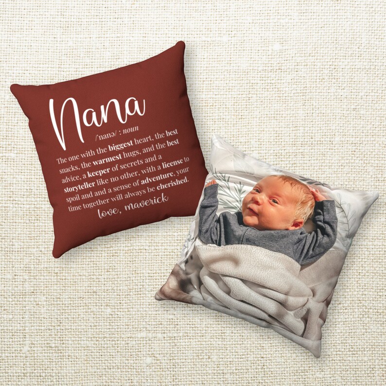 May include: A red throw pillow with white text that reads "Nana /nana/: noun The one with the biggest heart, the best snacks, the warmest hugs, and the best advice, a keeper of secrets and a storyteller like no other, with a license to spoil and a sense of adventure, your time together will always be cherished. love, maverick". The pillow is next to a white pillow with a photo of a baby.