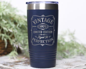 Könnte beinhalten: Ein marineblauer isolierter Becher mit einem silbernen Deckel. Der Becher trägt den Text "VINTAGE 1975 LIMITED EDITION Aged To Perfection" in Silber. Der zylindrische Becher hat ein geriffeltes Design.