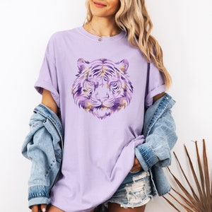 May include: A lavender t-shirt featuring a purple and gold tiger graphic. The tiger's face is centrally positioned on the shirt.