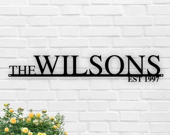 Puede incluir: Un letrero de metal negro con el texto "The Wilsons Est 1997" en una pared de ladrillo blanco.