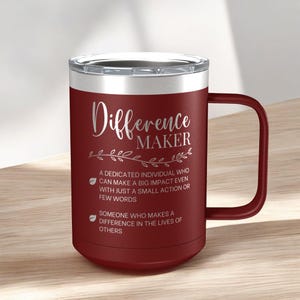 May include: A maroon stainless steel travel mug with a silver lid and a black handle. The mug has the text "Difference Maker" in silver lettering and a definition of the term below.