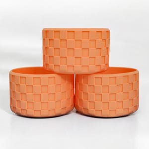 May include: Three orange ceramic planters with a checkered pattern. The planters are stacked on top of each other.
