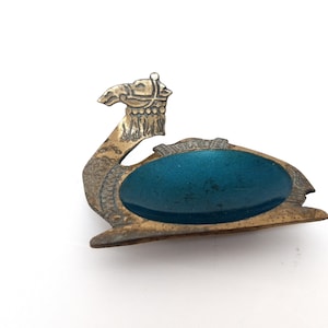 Puede incluir: Cenicero vintage en forma de camello de latón con una cubeta ovalada de esmalte turquesa. La cabeza del camello está detallada con una brida y elementos decorativos. La palabra "BISMUTH" es visible en el cenicero.
