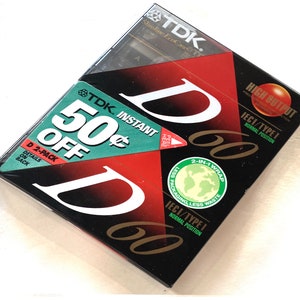 May include: A two-pack of TDK D60 audio cassette tapes. The packaging is black with red and white accents, featuring the TDK logo and the text "50&cent; OFF". The tapes are labeled "High Output" and "IECI/TYPE I".