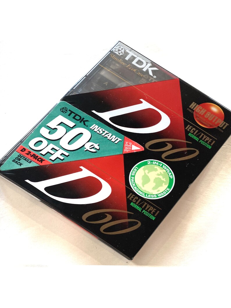 May include: A two-pack of TDK D60 audio cassette tapes. The packaging is black with red and white accents, featuring the TDK logo and the text "50&cent; OFF". The tapes are labeled "High Output" and "IECI/TYPE I".