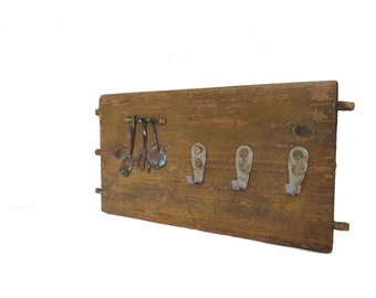 Kitchen wall reclaimed wood hook rack with brass cutouts and 3 rusty metal hooks.