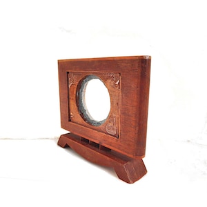 May include: A rectangular, wooden picture frame with a circular opening. The frame is a warm brown color and has a decorative base. The frame is designed to hold a circular object or image.