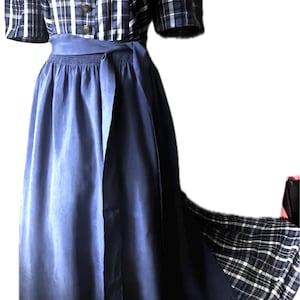 May include: A floor-length dress featuring a navy blue and white plaid bodice with short sleeves, a square neckline, and a row of dark buttons. The skirt is a solid navy blue with a matching tie-waist sash and a plaid panel visible at the hem.