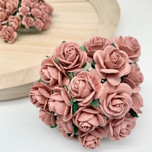 May include: A bunch of blush pink paper roses with green leaves. The roses are arranged in a circular shape and are ideal for adding a touch of elegance to any craft project.