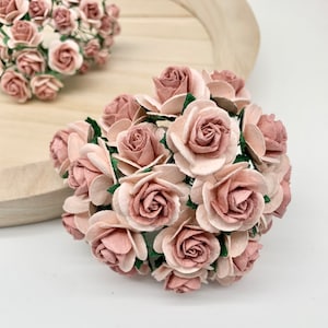 May include: A bunch of blush pink paper roses with green leaves. The roses are arranged in a bouquet shape.