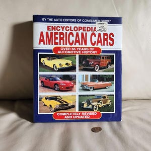 May include: A hardcover book titled "Encyclopedia American Cars" with images of classic cars. The cover is blue with red and white text, and features a collage of vintage vehicles. The book is "Completely Revised and Updated."