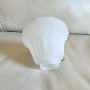 May include: A frosted glass lamp shade featuring a bell-shaped silhouette with vertical fluted ridges and a delicate embossed floral pattern near the top. The shade has a circular opening at the base and a smooth, translucent white finish throughout.