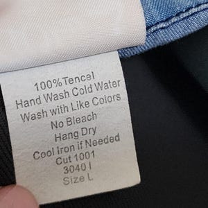 May include: A white clothing tag with black text, including care instructions: 100% Tencel, Hand Wash Cold Water, Wash with Like Colors, No Bleach, Hang Dry, Cool Iron if Needed. Also includes Cut 1001, 30401, and Size L.