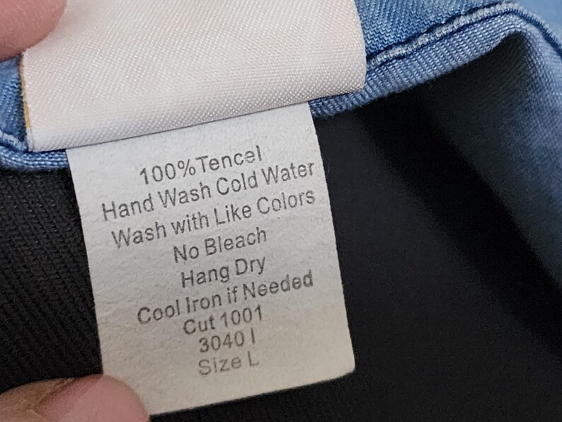 May include: A white clothing tag with black text, including care instructions: 100% Tencel, Hand Wash Cold Water, Wash with Like Colors, No Bleach, Hang Dry, Cool Iron if Needed. Also includes Cut 1001, 30401, and Size L.