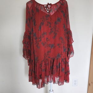 May include: A red dress with a floral design. The dress features long, flowing sleeves and a tiered, ruffled hem. The neckline is a scoop with a tie detail. The fabric is sheer and lightweight, ideal for warmer weather.