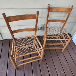 May include: Two antique wooden chairs with woven seats. The chairs have a light brown finish and a ladder-back design. The seats are made of woven natural fibers. The chairs are placed on a wooden deck.