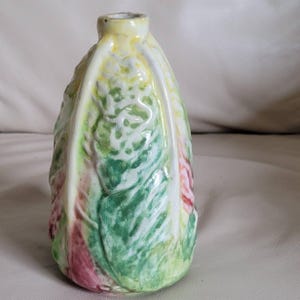 May include: A ceramic vase shaped like a head of cabbage with a glossy finish. The surface features textured, overlapping leaf patterns in shades of vibrant green, pale yellow, and muted pink, with a narrow, circular opening at the top.