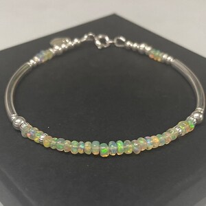 May include: A silver bracelet featuring a row of iridescent opal beads. The bracelet is displayed against a black background.