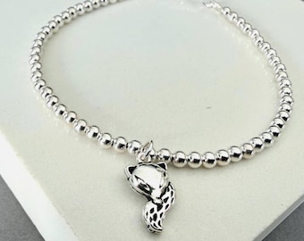Könnte beinhalten: Ein silbernes Perlenarmband mit einem fuchsformigen Anhänger. Das Armband besteht aus kleinen, polierten silbernen Kugeln, die aneinandergereiht sind, mit einem verstellbaren Schiebemechanismus oben und einem detaillierten Fuchskopf-Anhänger.