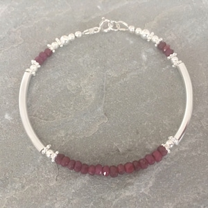 May include: A silver bangle bracelet with a row of small, dark red gemstone beads.