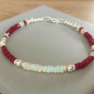 May include: A silver chain bracelet with red and white beads. The bracelet is made with small, round beads of red and white gemstones.
