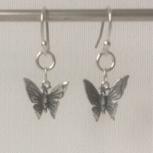 K&ouml;nnte beinhalten: Ein Paar silberfarbene Schmetterlingsohrringe. Jeder Ohrring hat einen detaillierten Schmetterlingsanh&auml;nger, der an einem Haken h&auml;ngt. Die Schmetterlingsfl&uuml;gel sind ausgebreitet und das Design ist aufwendig. Die Ohrringe werden vor einem schlichten Hintergrund gezeigt.