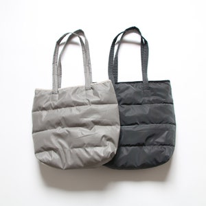 May include: Two quilted tote bags, one gray and one black. The bags have a simple design with a single handle.