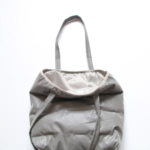 May include: A gray quilted tote bag with a light gray lining and two handles. The bag has a drawstring closure.