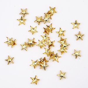 Può includere: Una spolverata di decorazioni dorate a forma di stella su uno sfondo bianco.