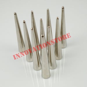 May include: A set of eight silver metal cone-shaped studs. The studs are arranged in a semi-circle on a white surface.
