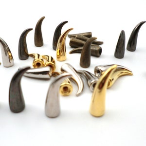 May include: A collection of small, decorative horns in gold, silver, and bronze finishes. The horns are made of metal and have a pointed tip. They are perfect for adding a touch of whimsy to any project.