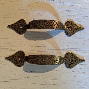 May include: Two antique brass cabinet pulls with a textured finish and a heart-shaped design. The pulls have a single hole for mounting.