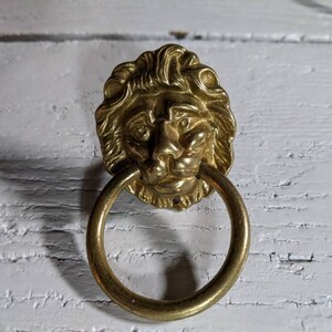 Op de afbeelding: Een gouden deurknop met een leeuwenkop en een ronde ring.