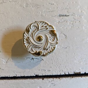 Op de afbeelding: Witte kastknop met een gouden bloemmotief.