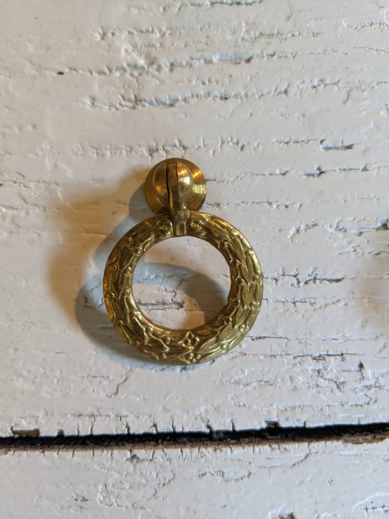 Op de afbeelding: Een gouden ringvormige kastknop met een bloemmotief.