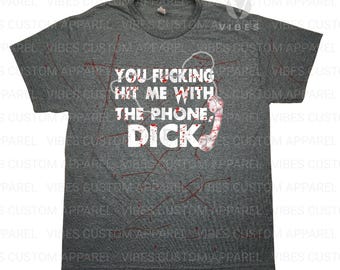 May include: Dark gray t-shirt with the text "YOU FUCKING HIT ME WITH THE PHONE, DICK" in white. The design includes a vintage telephone graphic and red splatter details.